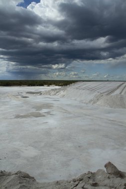 Endüstriyel Dramatik bir gökyüzünün altında doğal beyaz tuz düzlükleri ve açık maden ocağı manzarası.