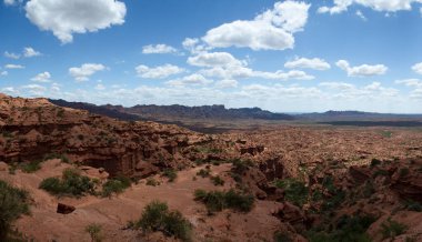 Kırmızı kanyon. Kurak çöl manzarası, kumtaşı ve kayalık uçurumlar ve bulutlu mavi gökyüzünün altındaki dağlar..