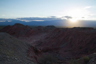 Kurak çöl manzarası, kumtaşı oluşumları, kayalık dağlar ve Arjantin 'in La Rioja kentindeki Talampaya milli parkında saklanan güneş gün batımında..