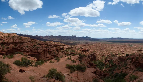 Kırmızı kanyon. Kurak çöl manzarası, kumtaşı ve kayalık uçurumlar ve bulutlu mavi gökyüzünün altındaki dağlar..