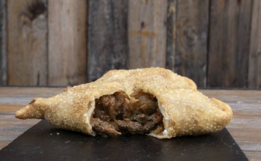 Parmak yiyeceği. Ahşap arka planda, siyah bir tabakta geleneksel kızarmış et böreğinin yakın görüntüsü.. 