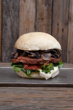 Vejetaryen mutfağı. Bitki bazlı gıda. Patates ekmekli, mantarlı, güneşte kurutulmuş domatesli, roka ve NotCo mayonezli olmayan hamburgerin yakın plan görüntüsü..