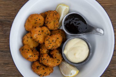 Deniz ürünleri. Tahta masanın üzerinde limon, aioli ve teriyaki soslu panko karidesli beyaz bir kâse..