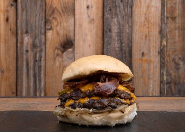 Canavar burgerler. İki et madalyonu, çedar peyniri, pastırma, ızgara soğan ve salatalıklı hamburgerin yakın görüntüsü..