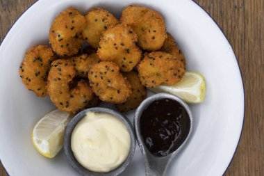 Deniz ürünleri. Tahta masanın üzerinde limon, aioli ve teriyaki soslu panko karidesli beyaz bir kâse..