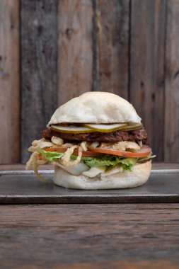 Vejetaryen mutfağı. Bitki bazlı burger. Burger değil. NotCo hamburgerin yakın plan görüntüsü. Domates, marul, çıtır soğan halkaları ve NotCo mayonez. Restorandaki ahşap tabakta..