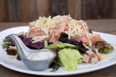 Marul, parmesan peyniri, kızarmış ekmek, somon, pastırma ve Sezar soslu Sezar salatası ahşap bir tabakta..