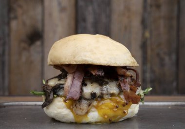 Ekmek, pastırma, çedar peyniri, marul, domates ve hardallı hamburger, ahşap arka planda..