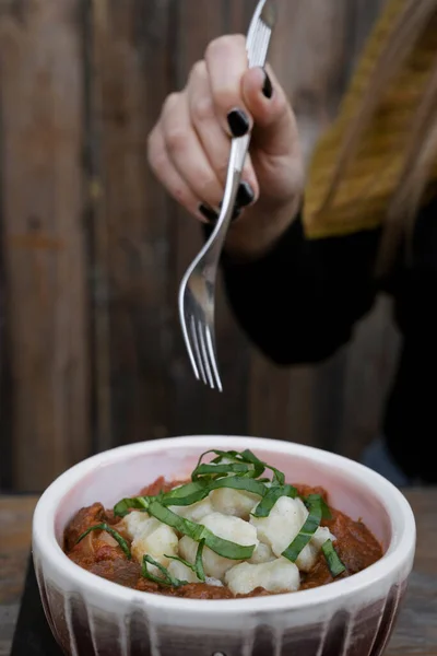 About to eat traditional Hungarian Goulash at the restaurant. Closeup view of a woman holding a fork, having goulash stew with veal and gnocchi, in a bowl.