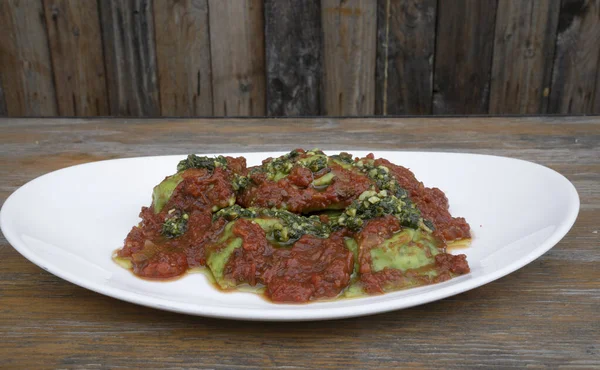 Pasta. Closeup view of spinach ravioli with tomato sauce and pesto, in a white dish on the wooden table.
