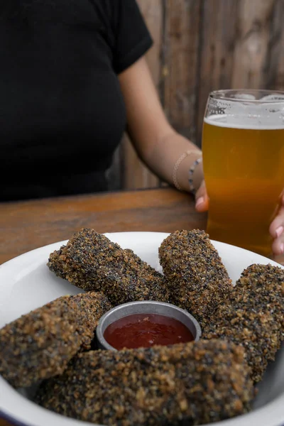 Vegan cuisine. View of a woman having a glass of beer and vegan mozzarella sticks and quinoa with a sweet chili dipping sauce.