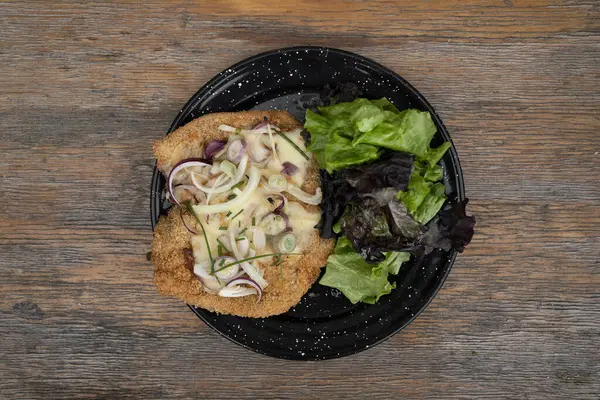 Milanesa 'nın en iyi manzarası, ekmek kırıntılı sığır eti ve restoran masasındaki siyah tabakta taze bir salata.. 