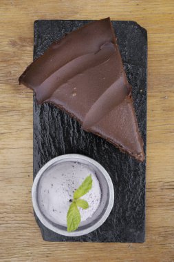 Tatlılar. Bir dilim çikolatalı pastanın üstünde siyah bir tabakta dondurmayla ahşap masa..