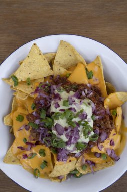 Acı biberli cips. Çedar peynirli nachos, avokado kremi, kırmızı soğan turşusu ve ahşap arka planlı beyaz kasede et sosu..