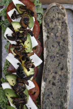 Vejetaryen sandviç. Domatesli, vejetaryen mozzarella, lahana, avokado, babaganoush ve mantar cipsli vejetaryen baget, ahşap bir tabakta..