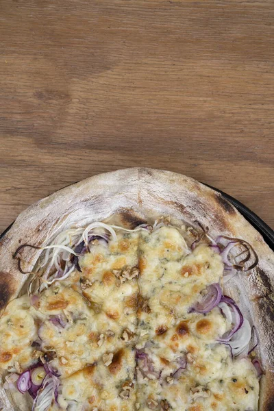 stock image Top view of a homemade pizza with cheese and red onion, in a pizza pan on the wooden table. 