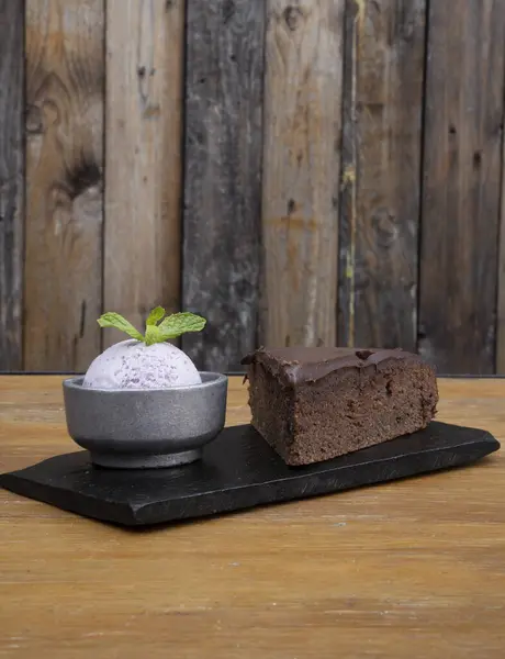 Bakery and desserts. Closeup view of a slice of chocolate cake with ice cream in a black dish on the wooden table.