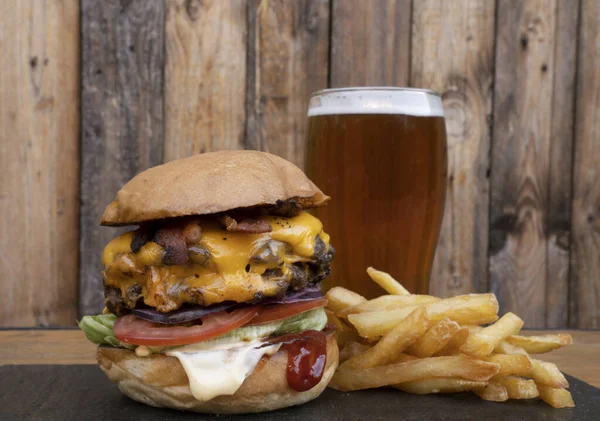 Food and drink. closeup view of a giant burger with two meat medallions, cheddar cheese, tomato, lettuce, mayonnaise, ketchup, french fries and a pint of beer.
