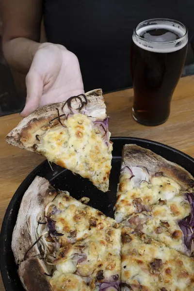 Eating pizza at the restaurant. Closeup view of a woman\'s hand holding a slice of pizza with mozzarella, provolone cheese and onions.