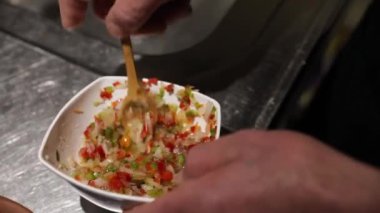 Gastronomi. Erkek aşçı elleri, mutfakta kreol salatasını farklı biberlerle ve dilimlenmiş soğanla karıştırıyor..