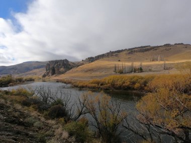 Idyllic Alp arazisi. Altın vadi ve dağlardan akan nehrin manzarası. Saf su akıntısı, sarı çayırlar, sonbaharda tepeler ve kaya oluşumu..