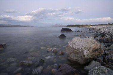 Gün batımında Nahuel Huapi Gölü 'nün uzun pozu. Güzel bulanık su efekti, kayalık kıyı ve alacakaranlık rengi.