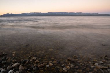 Gün batımında Nahuel Huapi Gölü 'nün uzun pozu. Güzel bulanık su efekti, kayalık kıyı ve alacakaranlık rengi.