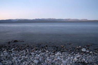 Gün batımında Nahuel Huapi Gölü 'nün uzun pozu. Güzel bulanık su efekti, kayalık sahil ve ufuktaki And Dağları sihirli bir alacakaranlık ışığıyla.