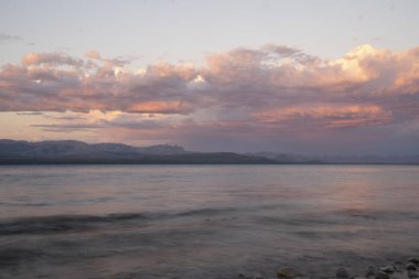 Gün batımında Nahuel Huapi Gölü ve And Dağları 'nın uzun pozlu görüntüleri. Güzel bulanık su efekti, kayalık kıyı ve alacakaranlık rengi gökyüzünde.