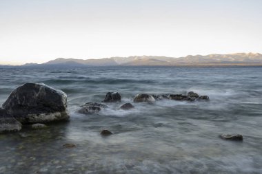 Gün batımında Nahuel Huapi Gölü 'nün uzun pozu. Güzel bulanık su efekti, kayalık kıyı ve alacakaranlık rengi.