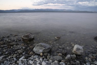 Gün batımında Nahuel Huapi Gölü 'nün uzun pozu. Güzel bulanık su efekti, kayalık kıyı ve alacakaranlık rengi.