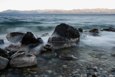 Gün batımında Nahuel Huapi Gölü 'nün uzun pozu. Güzel bulanık su efekti, kayalık kıyı ve alacakaranlık rengi.