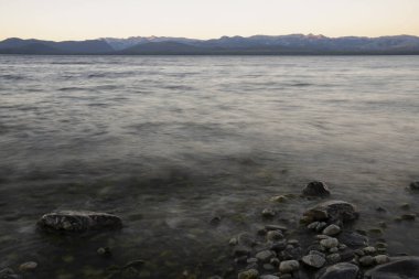 Gün batımında Nahuel Huapi Gölü ve And Dağları 'nın uzun pozlu görüntüleri. Güzel bulanık su efekti, kayalık kıyı ve alacakaranlık rengi gökyüzünde. 