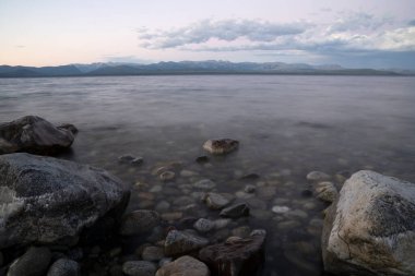 Gün batımında Nahuel Huapi Gölü ve And Dağları 'nın uzun pozlu görüntüleri. Güzel bulanık su efekti, kayalık kıyı ve alacakaranlık rengi gökyüzünde. 