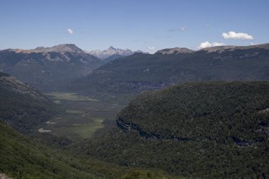 Dağları, vadiyi ve yeşil ormanı, berrak mavi gökyüzünün altında.