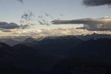 Gün batımında bulutlu bir gökyüzünün altında dağları ve ormanı görüyorum.. 