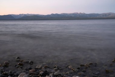 Gün batımında Nahuel Huapi Gölü 'nün uzun pozu. Güzel bulanık su efekti, kayalık sahil ve ufuktaki And Dağları sihirli bir alacakaranlık ışığıyla.