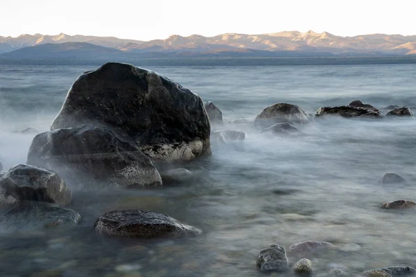 Gün batımında Nahuel Huapi Gölü 'nün uzun pozu. Güzel bulanık su efekti, kayalık kıyı ve alacakaranlık rengi.