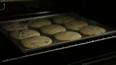 Kadın fırını açıp tavadaki çikolatalı kurabiyeleri kontrol ediyor.