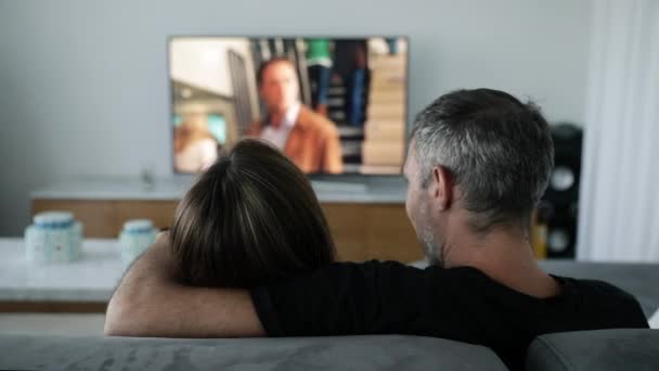 一对浪漫的年轻夫妇坐在沙发上看电视里的电影 他们互相交谈 互相拥抱 — 图库视频影像