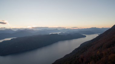 Tepenin tepesinden büyüleyici bir manzara. Gün batımında ormanın, gölün, vadinin ve dağların manzarası. 