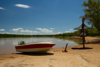 Panorama view of the river shore in a summer sunny day. A boat in the sand in the foreground and the tropical jungle in the background reflected in the water. clipart