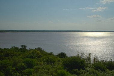Güneş doğarken yeşil tropikal orman ve Parana nehri manzarası. Güneşin su yüzeyindeki yansıması.