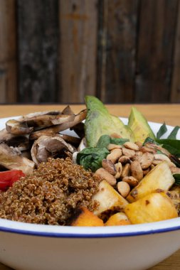 Vejetaryen mutfağı. Dilimlenmiş avokado, ızgara balkabağı, kinoa, mantar, kiraz domatesleri ve ahşap bir kasede kavrulmuş kestane kestanesi ile taze salatanın yakın görüntüsü..