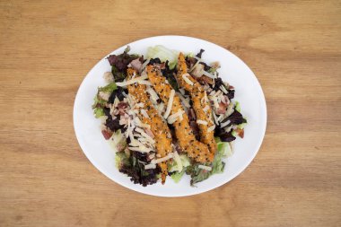 Sezar salatası. Taze salata, marul, parmesan peyniri, ekmek kırıntısı, susamlı kızarmış tavuk ve ahşap bir tabakta kızarmış domuz pastırması..