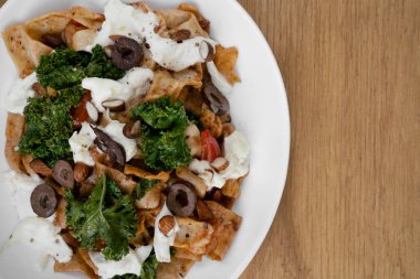 Makarna tabağı. Restoranın ahşap masasında pappardelle noodle, pesto, badem, lahana, burrata peyniri ve domatesli tabağın üst görüntüsü..