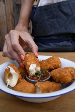 Kafkas bir kadının elinin yakından görüntüsü, kızarmış mozzarella çubuğunu kırmızı baharatlı sosa batırıyor, restoranda..