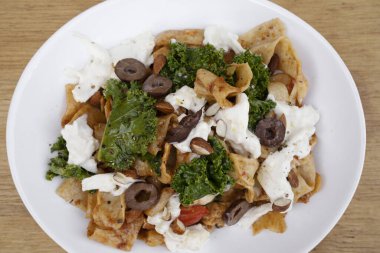 Makarna tabağı. Restoranın ahşap masasında pappardelle noodle, pesto, badem, lahana, burrata peyniri ve domatesli tabağın üst görüntüsü..