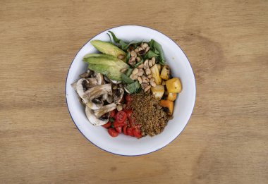 Vejetaryen mutfağı. Dilimlenmiş avokado, ızgara balkabağı, kinoa, mantar, kiraz domatesleri ve ahşap masada kavrulmuş kestane ile taze bir salata..