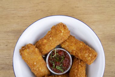 Gastronomi. Kırsal sunum. Kızarmış mozzarella peynirinin üst görüntüsü baharatlı soslu, ahşap masadaki beyaz kasede.. 